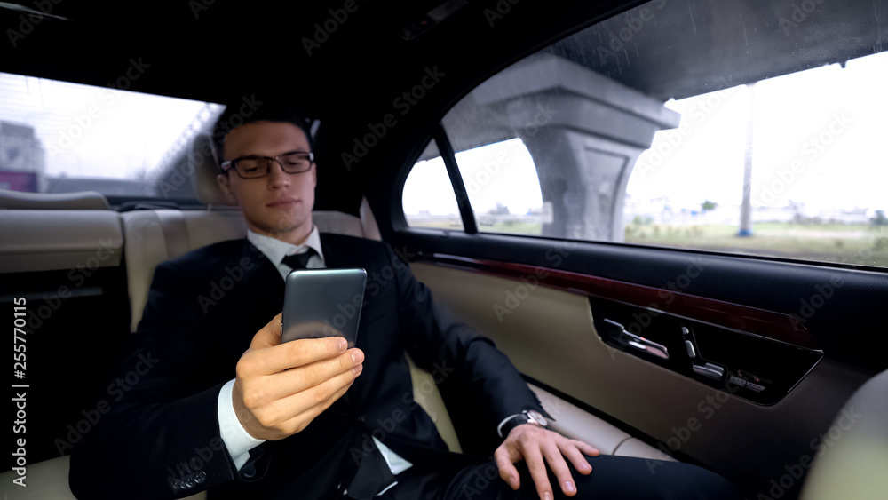 Pensive businessman writing e-mail, riding in car, stressful job, workaholic Pensive businessman writing e-mail, riding in car, stressful job, workaholic