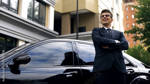 Happy young male standing by new luxurious car, office worker getting promotion © motortion