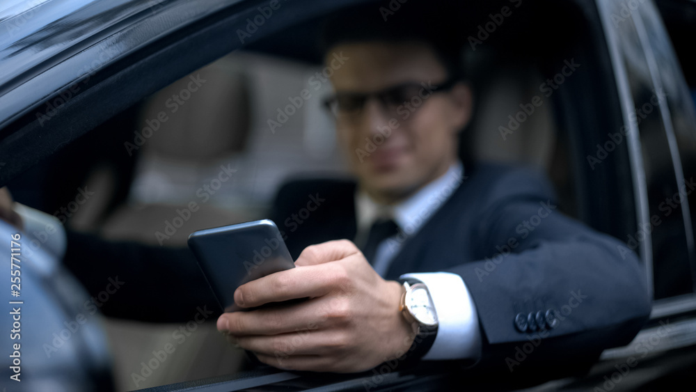 Man in business clothes texting on smartphone and smiling, sitting in auto
