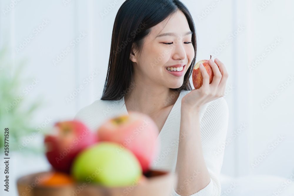 healthy beautiful attractive long black hair woman happiness smile hand hold red apple with foreground of fruit bowl white room interior background healthy beautiful attractive long black hair woman happiness smile hand hold red apple with foreground of fruit bowl white room interior background