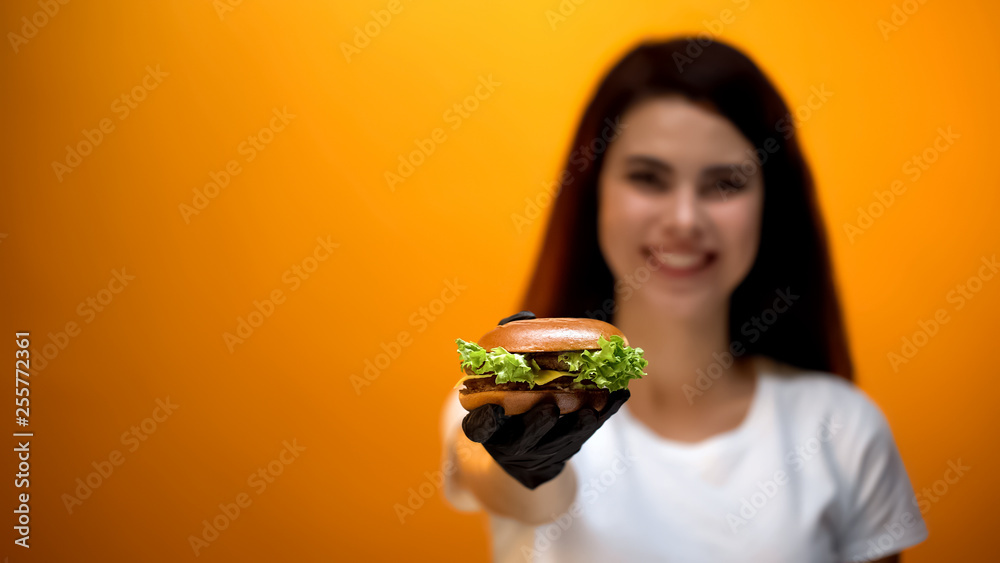 Girl in glove showing burger to camera, tasty fast food, good quality service Girl in glove showing burger to camera, tasty fast food, good quality service