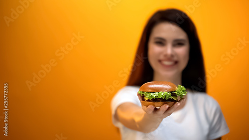 Happy girl showing hamburger to camera  satisfied client of fast food restaurant