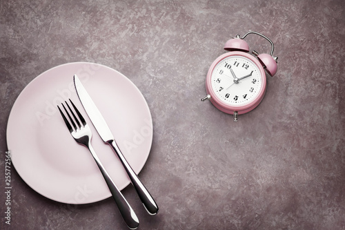 Alarm clock and plate with cutlery. Concept of intermittent fasting, lunchtime, diet and weight loss
