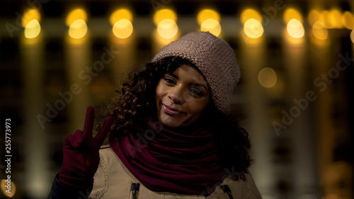 Young optimistic model posing at camera and showing victory hand sign, peace