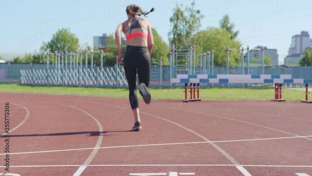 Rear view tilt up of unrecognizable female athlete preparing for run in starting position and beginning to sprint on track Rear view tilt up of unrecognizable female athlete preparing for run in starting position and beginning to sprint on track