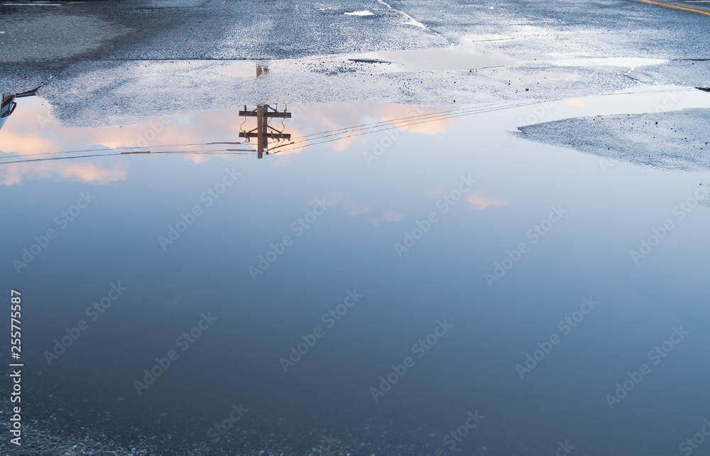 Puddle water reflection of sky clouds and power line. Above ground electricity pole reflected in urban setting background. Parking lot with abstract water puddle reflection Puddle water reflection of sky clouds and power line. Above ground electricity pole reflected in urban setting background. Parking lot with abstract water puddle reflection