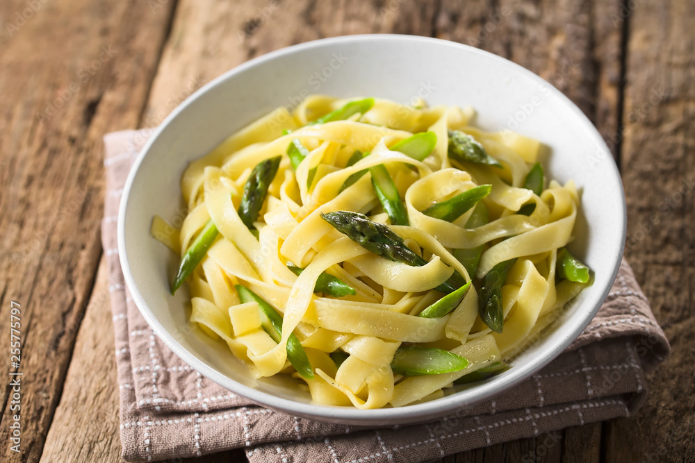Fresh homemade pasta dish of fettuccine or tagliatelle, green asparagus, garlic and lemon juice in bowl (Selective Focus, Focus on the asparagus head in the middle)
