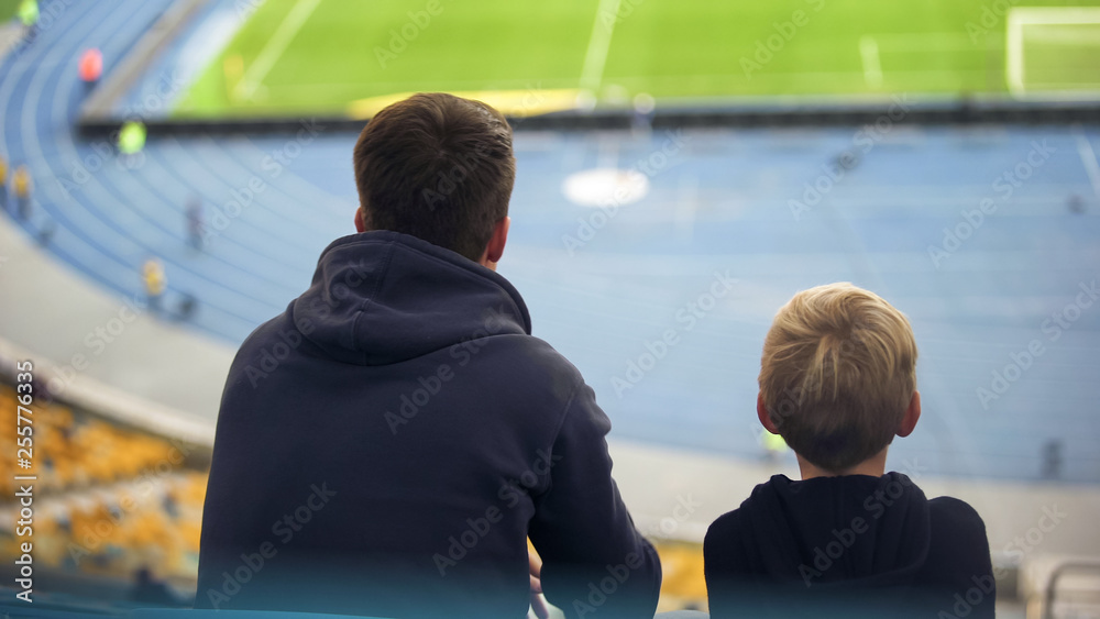 Boy with father sitting tribune at empty stadium, football fans on excursion
