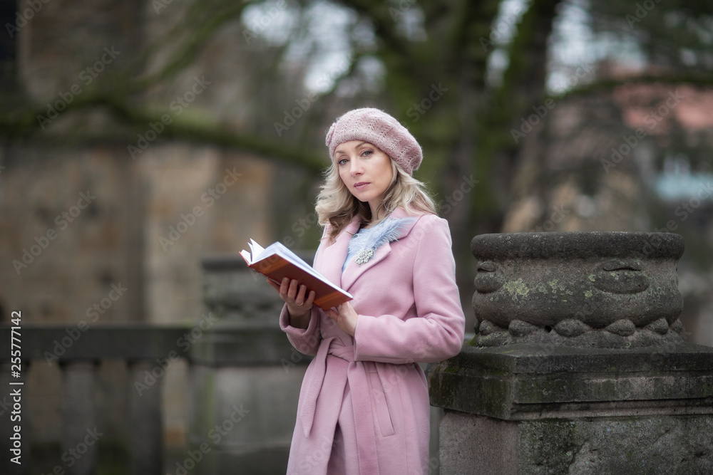 Naklejka premium Spring portrait of a girl reading a book in the Park.Female portrait.Blonde in pink.