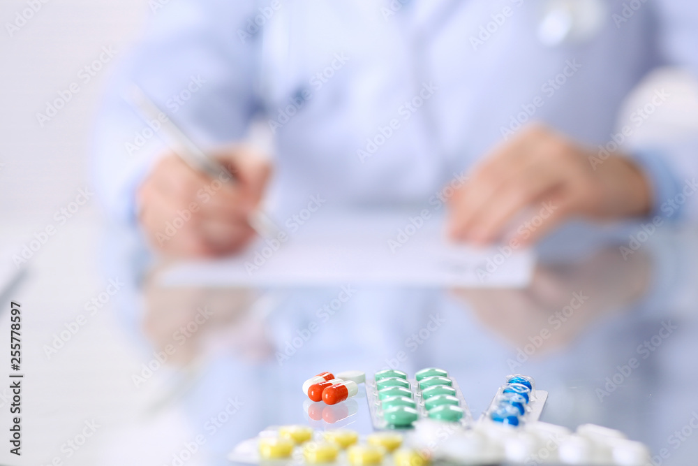 Unknown woman doctor at work at hospital. Pills at glass table. Young female physician write prescription or filling up medical form while sitting in hospital office, close-up Unknown woman doctor at work at hospital. Pills at glass table. Young female physician write prescription or filling up medical form while sitting in hospital office, close-up