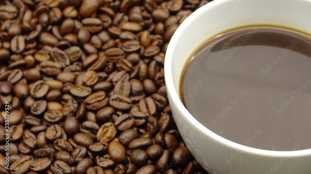 A cup of black coffee over roasted coffee beans