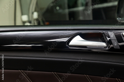 A close-up view of a part of the interior of a modern luxury car with a view of a silver-colored door handle on a chrome finish with black wood trim