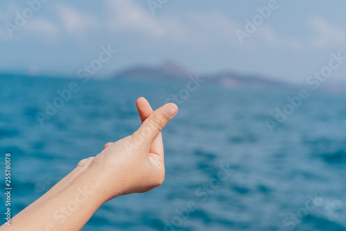 Mini heart, love symbolic at sea blue sky. Female hand isolated on white background. White woman's hand showing symbols and gestures. Korean mini heart finger sign. Asian symbol hand heart. Korean, Ch © Sumstudio
