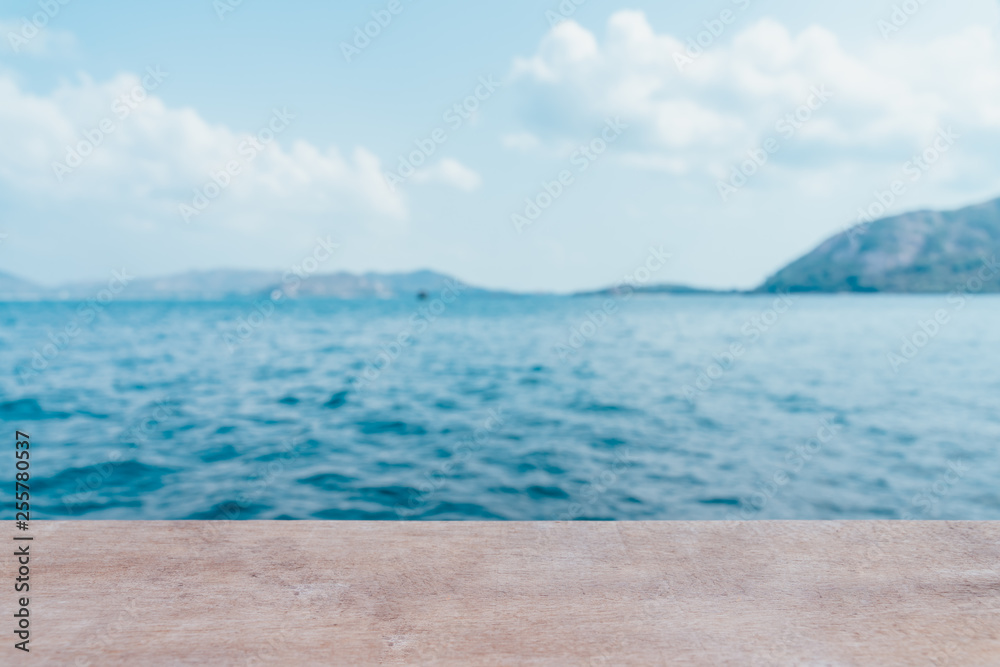 Empty wooden table with party on beach blurred background in summer time. The blur cool sea background with wood floor foreground on horizon tropical sandy beach; relaxing outdoors vacation with heave