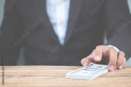 Close up hand of businessman holding money dollar bills on wooden table. Using as concept of corruption , Business corruption, bribe. With copy space for your text.