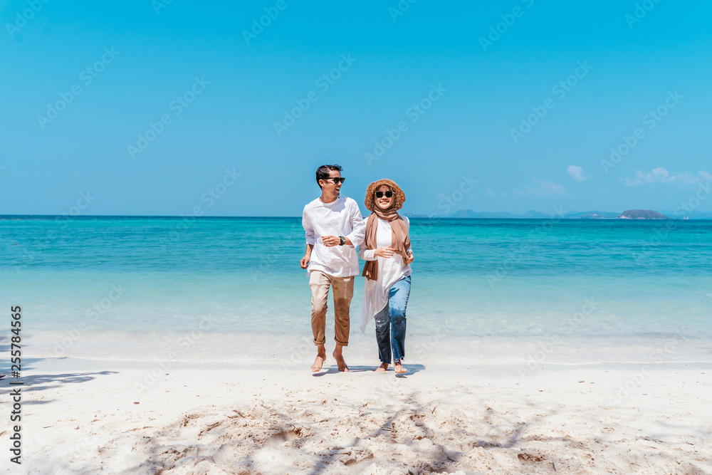 Young happy muslim couple white dress on running seashore. Travel Vacation Retirement Lifestyle Concept. young couple running together on the beach in vacation day. summer time.