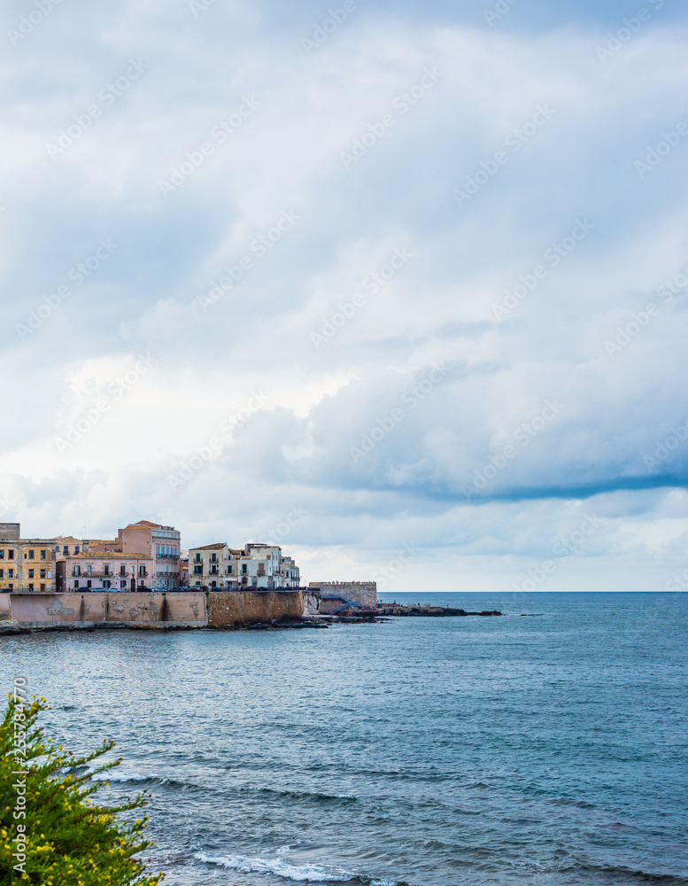 Wonderful view of the seafront of Ortigia in Syracuse on a summer day, with blue sea and cloudy sky as a backdrop.