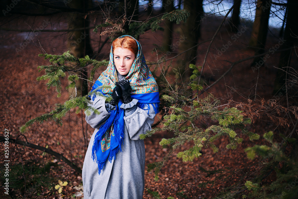 Portrait of a beautiful young girl of European appearance with red hair and blue eyes in the forest. Bright woman in the national scarf in nature. Illustration to a fairy tale or book. Russian beauty Portrait of a beautiful young girl of European appearance with red hair and blue eyes in the forest. Bright woman in the national scarf in nature. Illustration to a fairy tale or book. Russian beauty