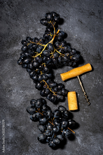 bunch of fresh grapes and a corkscrew on a dark background