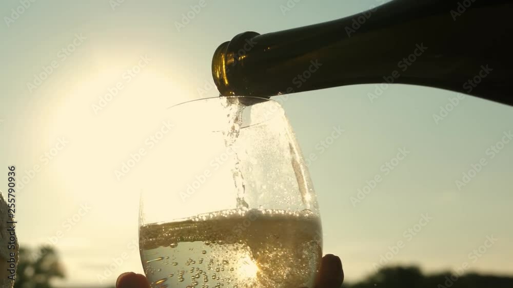 pour sparkling wine from bottle into transparent wine glasses against