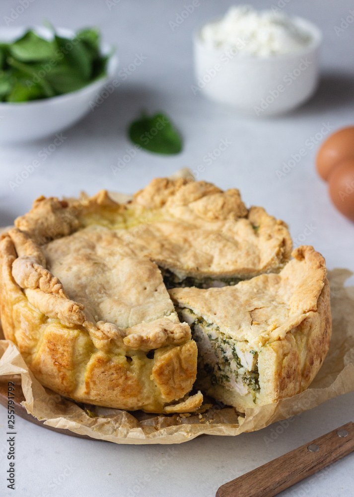 Spinach, chicken and ricotta pie with fresh spinach leaves, ricotta and eggs on a light stone background.