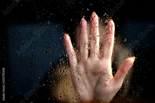 Female hand palm silhouette behind the window with raindrops reaching for the glass. A request for help, depression, stress blurred bokeh background. Refusal  denial of alcohol and drugs