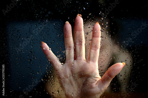 Female hand palm silhouette behind the window with raindrops reaching for the glass. A request for help  depression  stress blurred bokeh background. Refusal  denial of alcohol and drugs