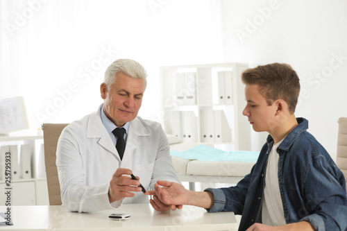 Doctor taking patient's blood sample with lancet pen in hospital. Diabetes control