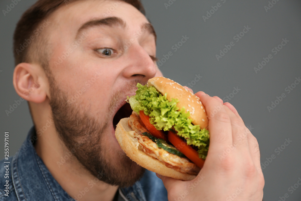 Young man eating tasty burger on grey background Young man eating tasty burger on grey background