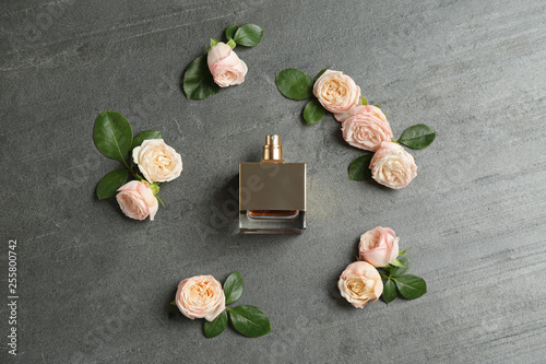Beautiful composition with bottle of perfume and roses on grey background, flat lay