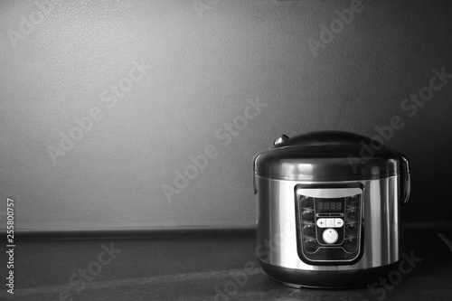 Modern multi cooker on table near black wall, space for text
