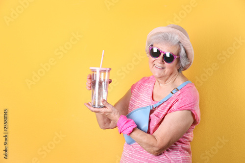Portrait of cool grandmother with drink on color background, space for text