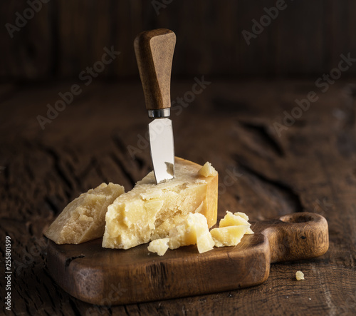 Piece of Parmesan cheese and cheese knife on the wooden board. Dark background.