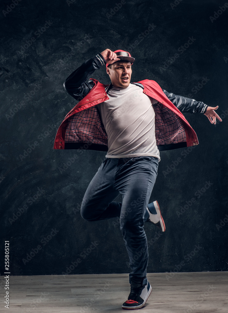 Stylish guy performs breakdance acrobatic elements. Studio photo against a dark textured wall