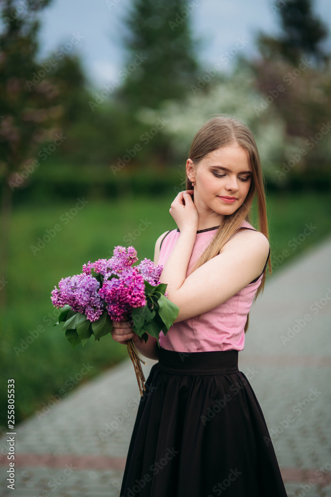 Fototapeta premium Attractive blond hair girl hold a bouquet of lilac in hands. Charming girl outside