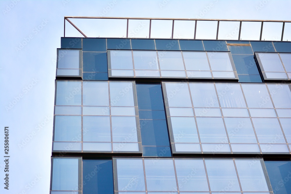 Fototapeta premium New office building in business center. Wall made of steel and glass with blue sky. 