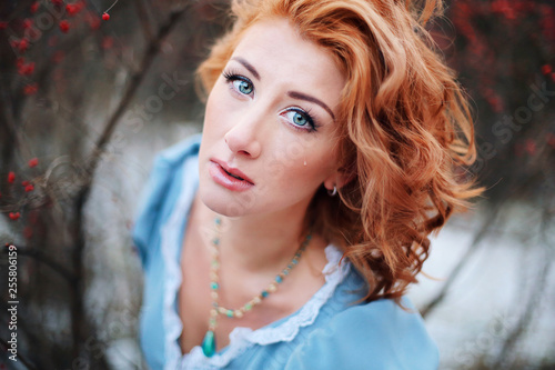 Beautiful young sad girl with red hair and blue eyes in an old dress with a deep look. European-looking woman with tears on. Bright sensual charming woman crying. Illustration of a fairy tale.