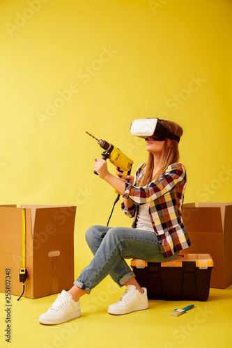 Girl in VR glasses doing repairs sitting on a tool box. Studio