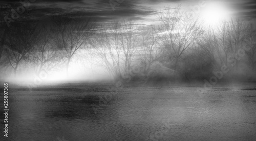 Background scene of empty street. Night view of the river, night sky with clouds, silhouettes of trees, light reflected on water. Smoke fog