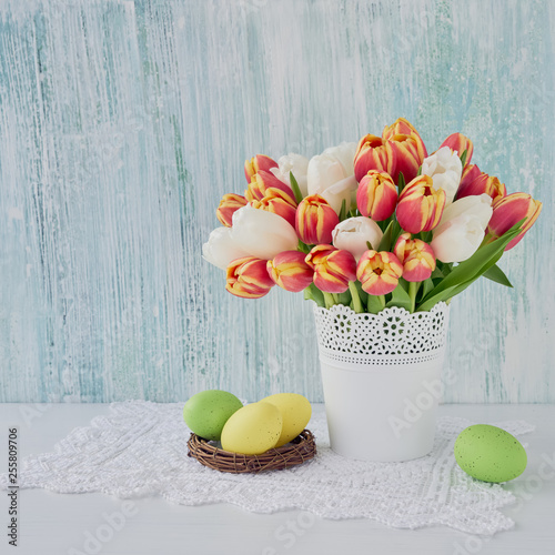 Easter background. Decorative Easter eggs and red tulips in vase. Copy space