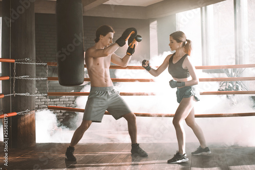 Boxing workout. Couple man and woman boxing together in the boxing ring at the gym. Sport box exercise two people. Man trainer in boxing gloves, woman in boxing bandages.