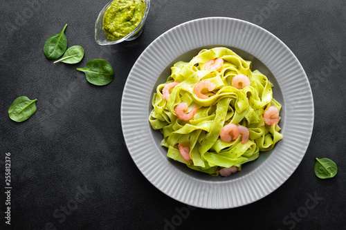 Boiled fettuccine pasta with fresh spinach pesto and shrimps on black background. Italian cuisine. Healthy dish for lunch. Top view