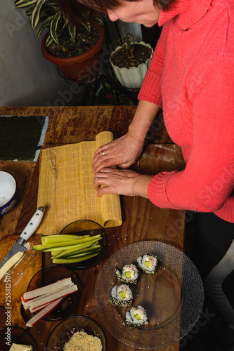 A female cook prepares sushi in the kitchen and wraps a letter to the nori in the roll photo