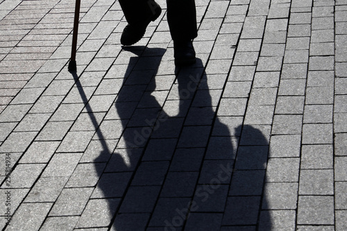 Schilderij op canvas Silhouette of man walking with a cane, long shadow on pavement