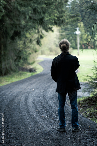Young man standing on road at end of dark forest
