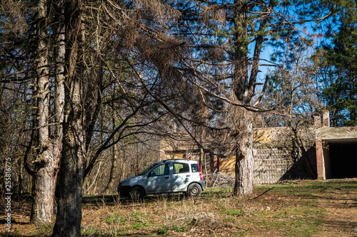 Small car parked in the forest by the ruins of the old building