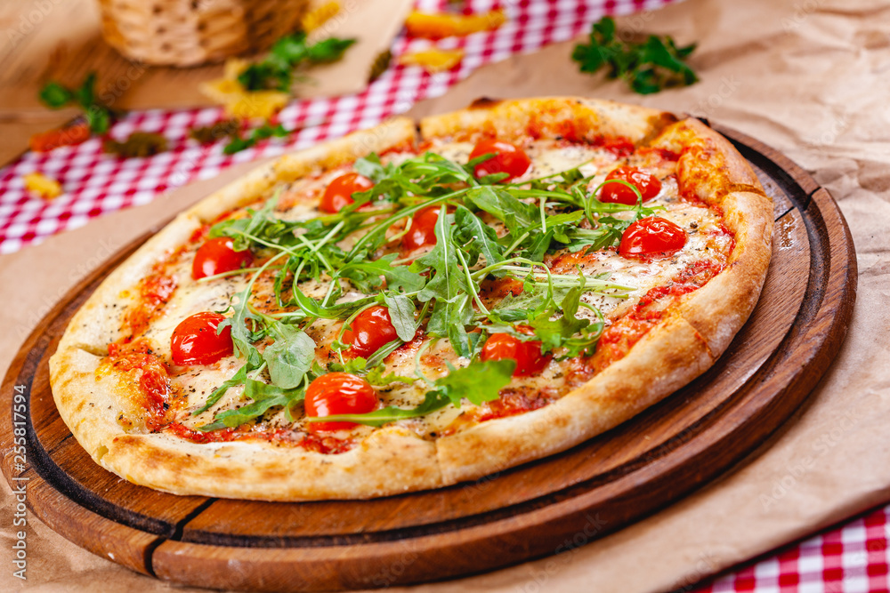Italian Pizza with tomatoes, mozzarella cheese and arugula on wooden cutting board. Close up