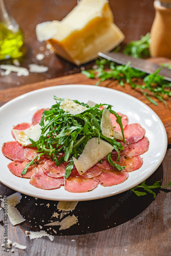 Meat carpaccio with arugula and parmesan cheese on white plate. Close up Meat carpaccio with arugula and parmesan cheese on white plate. Close up