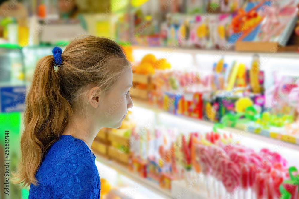 A girl stands at the shop window and looks at sweets and sweets.