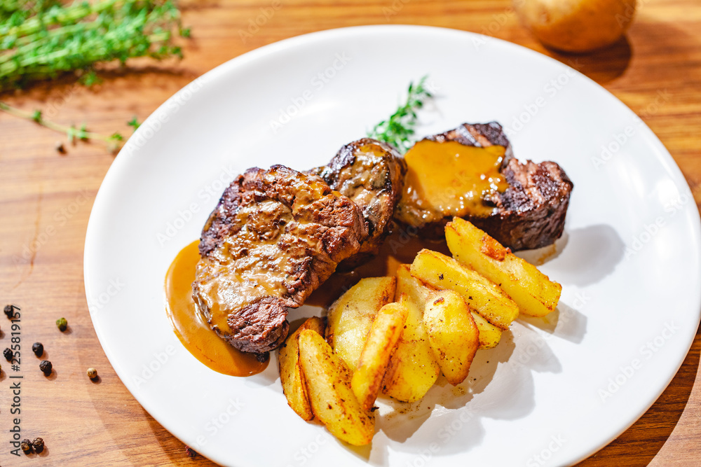 Grilled beef steak with potato wedges on white plate. Close up Grilled beef steak with potato wedges on white plate. Close up